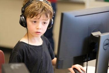 A young student sits at a computer with headphones